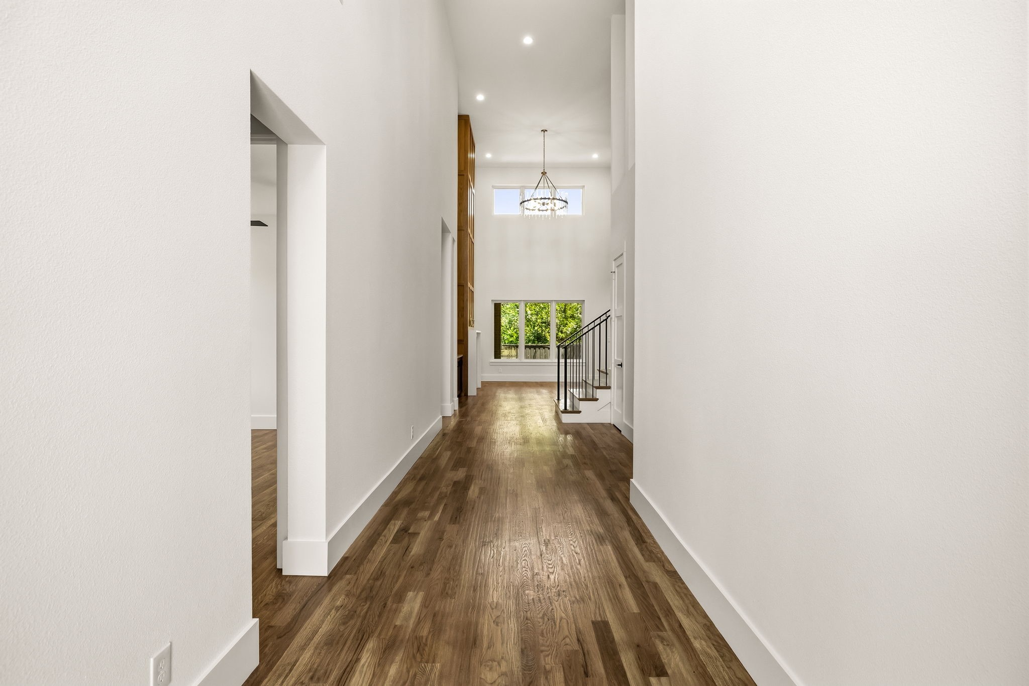 Empty entry hall with wood floors, a black-railed staircase, and a chandelier beneath high windows.