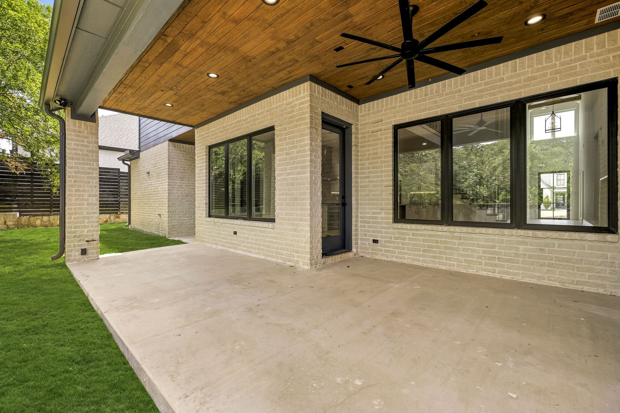 Covered brick patio with a wood ceiling, large windows, and a black ceiling fan.