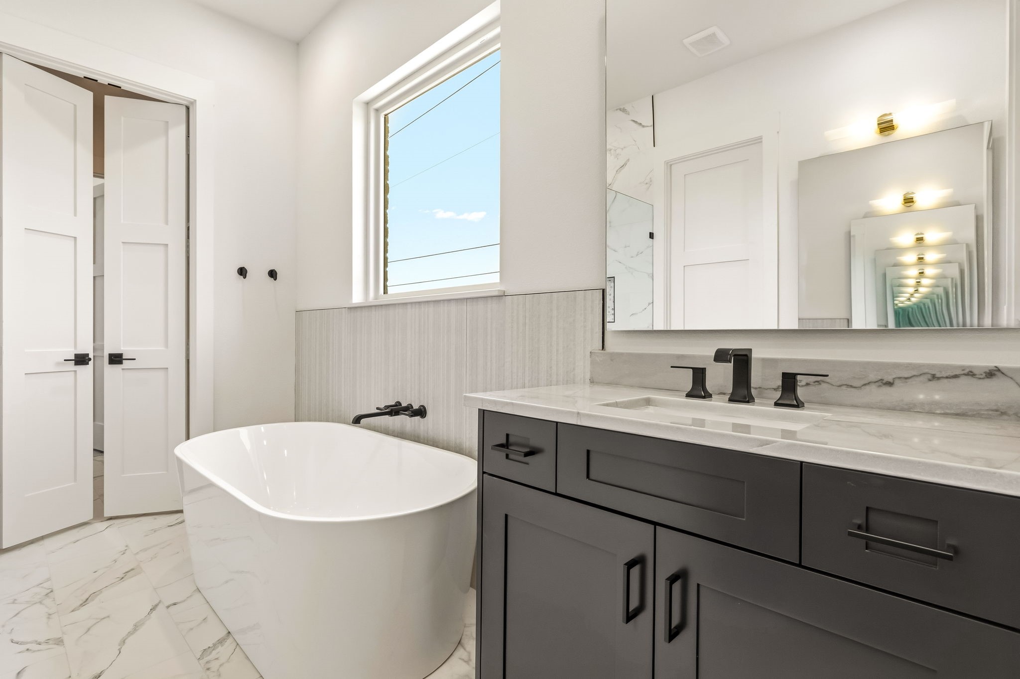 Modern bathroom with a freestanding soaking tub, dark vanity, marble-look surfaces, and large mirror.