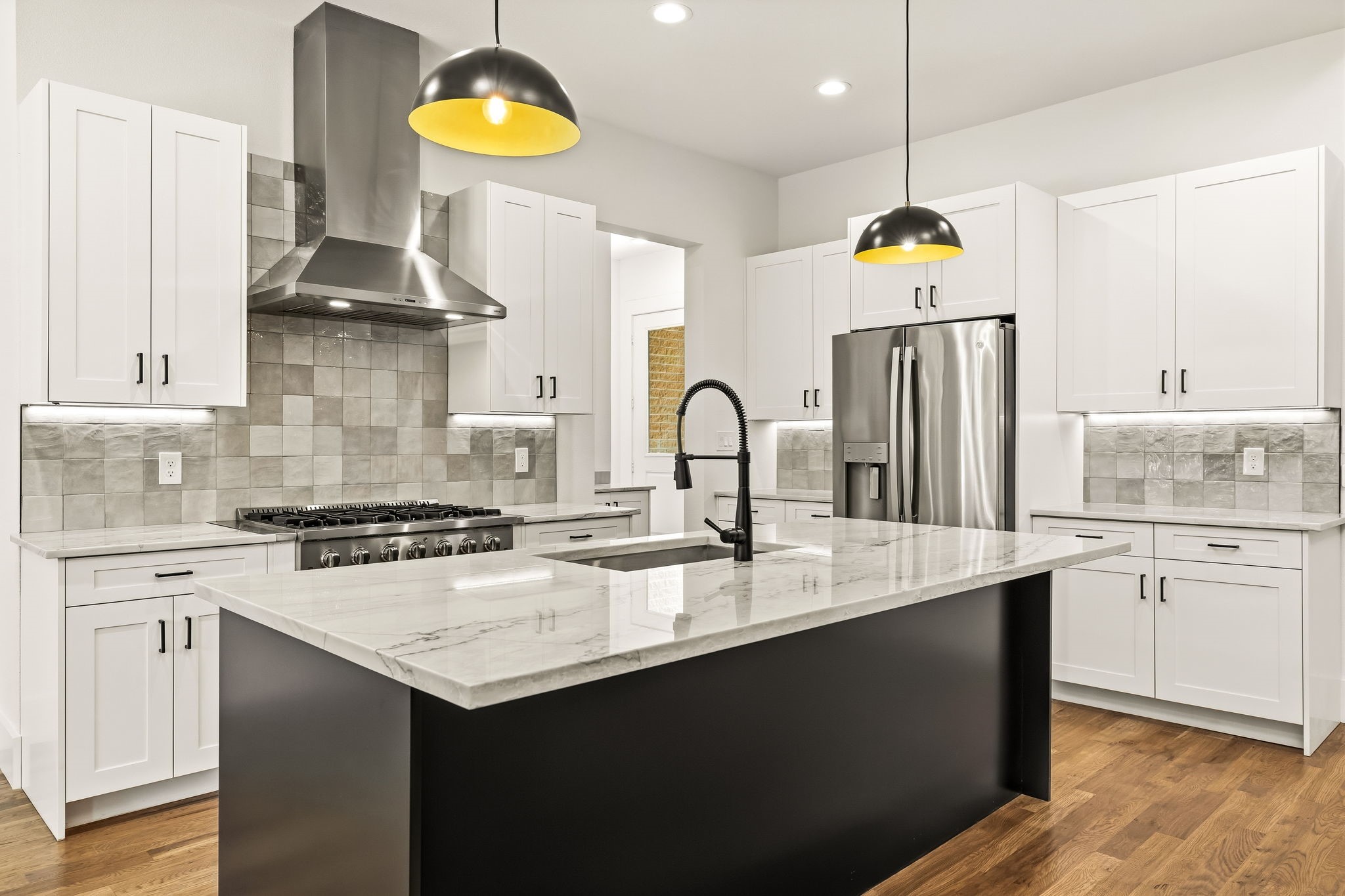 Modern kitchen with a large black island, marble countertop, white cabinets, and stainless steel appliances.