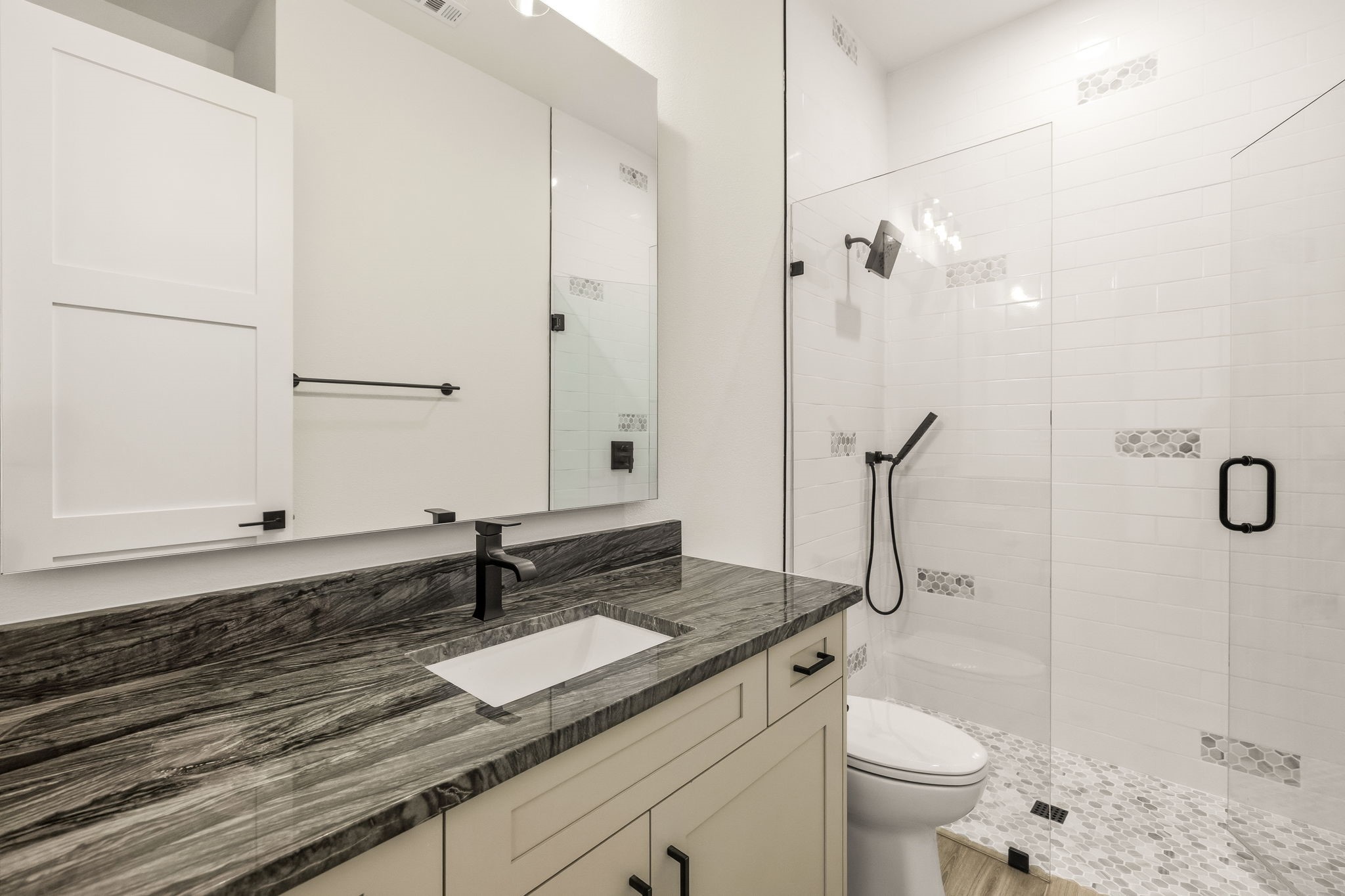 Modern bathroom with a gray stone vanity and glass-enclosed white-tiled shower.