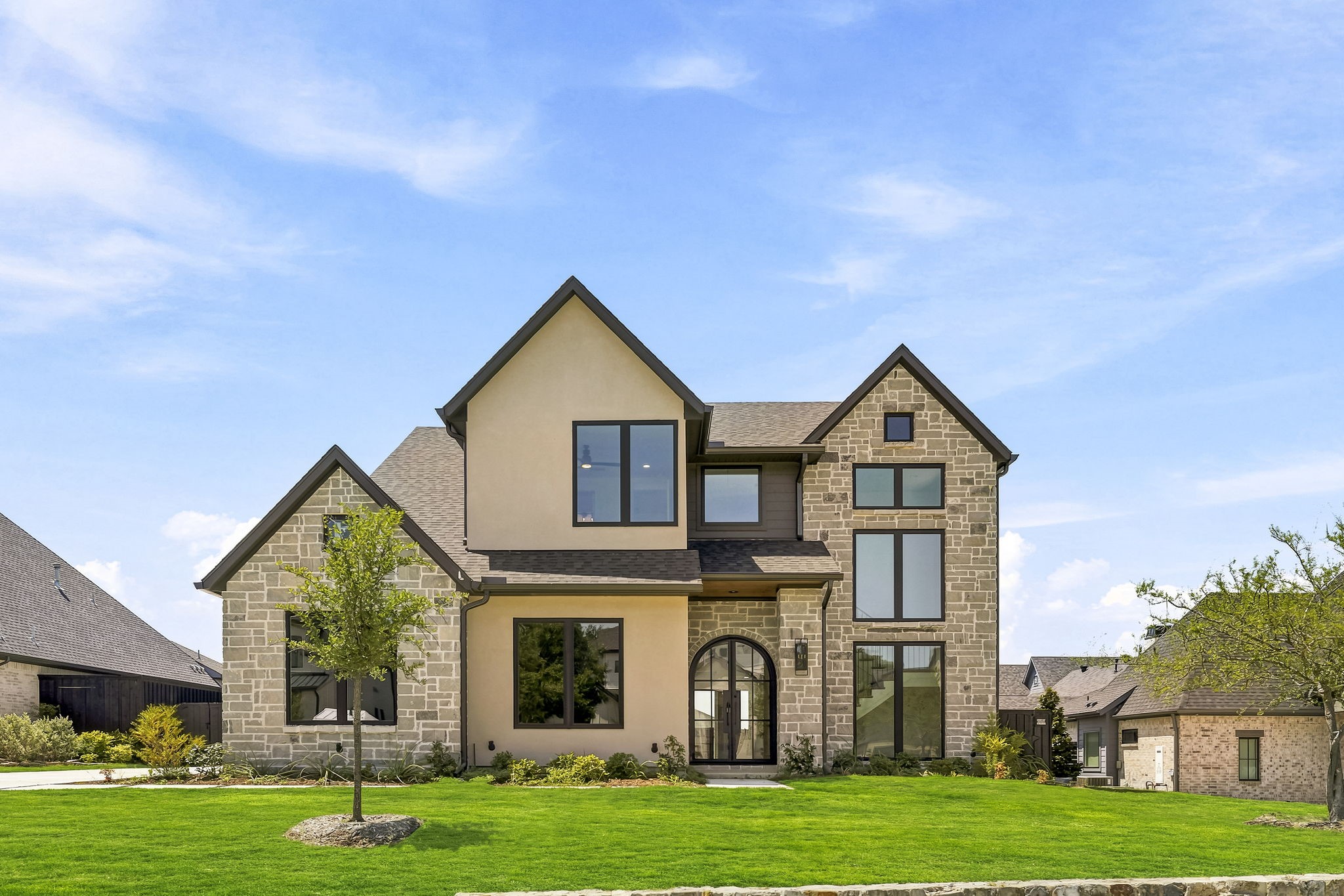 Two-story house with a stone-and-stucco facade, arched entry, and broad green lawn.