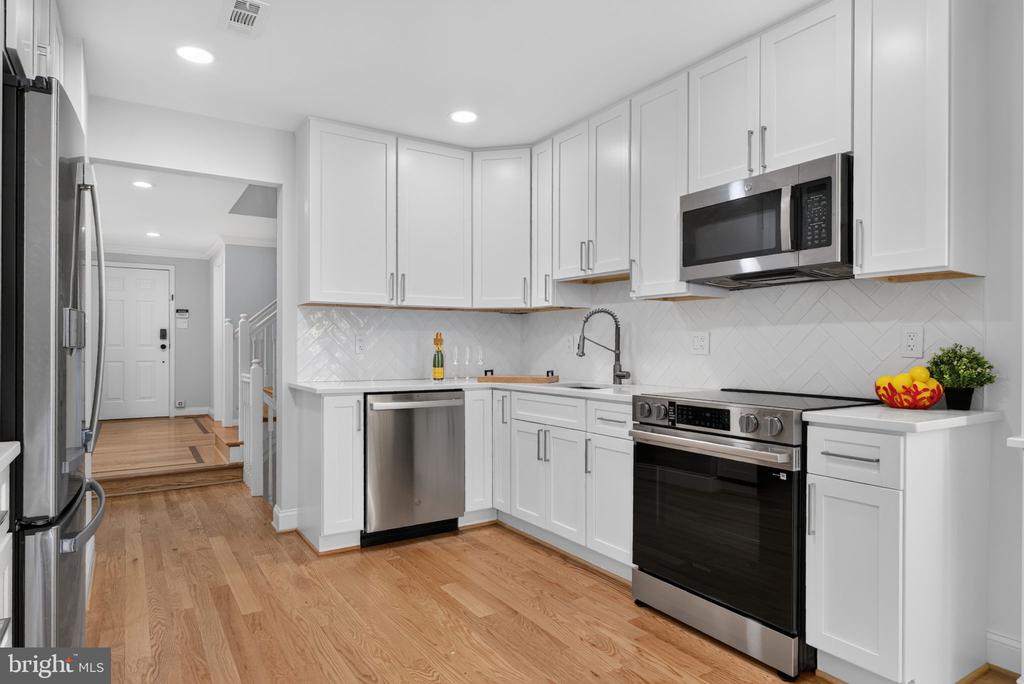 Kitchen with white cabinetry, stainless steel appliances, herringbone backsplash, and hardwood floors.