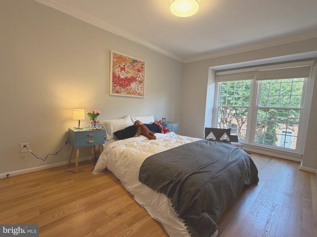 Bedroom with a white-and-charcoal bed, blue bedside tables, and wide windows overlooking trees.