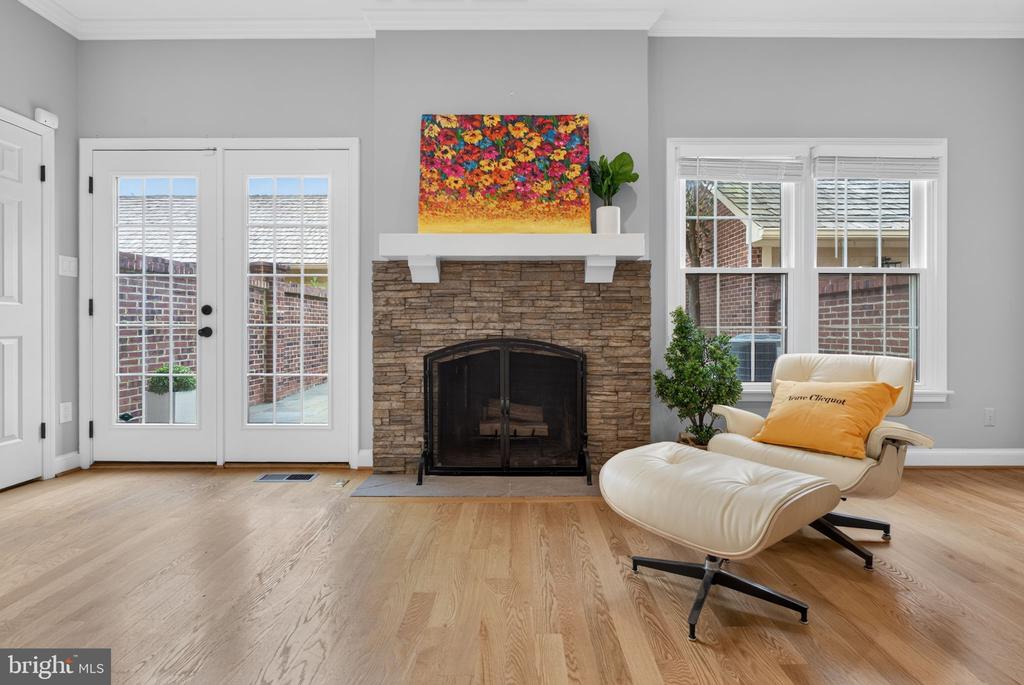 Living room with a stone fireplace, French doors, and a cream lounge chair and ottoman.