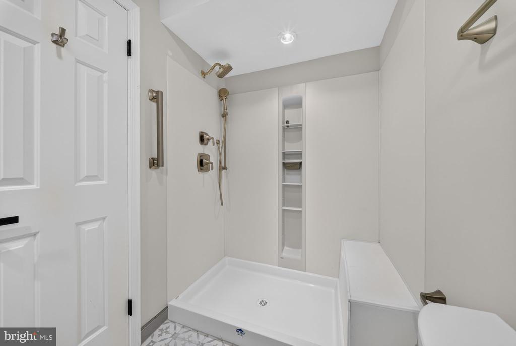 Walk-in shower with built-in niche, handheld showerhead, grab bars, and white shower base.