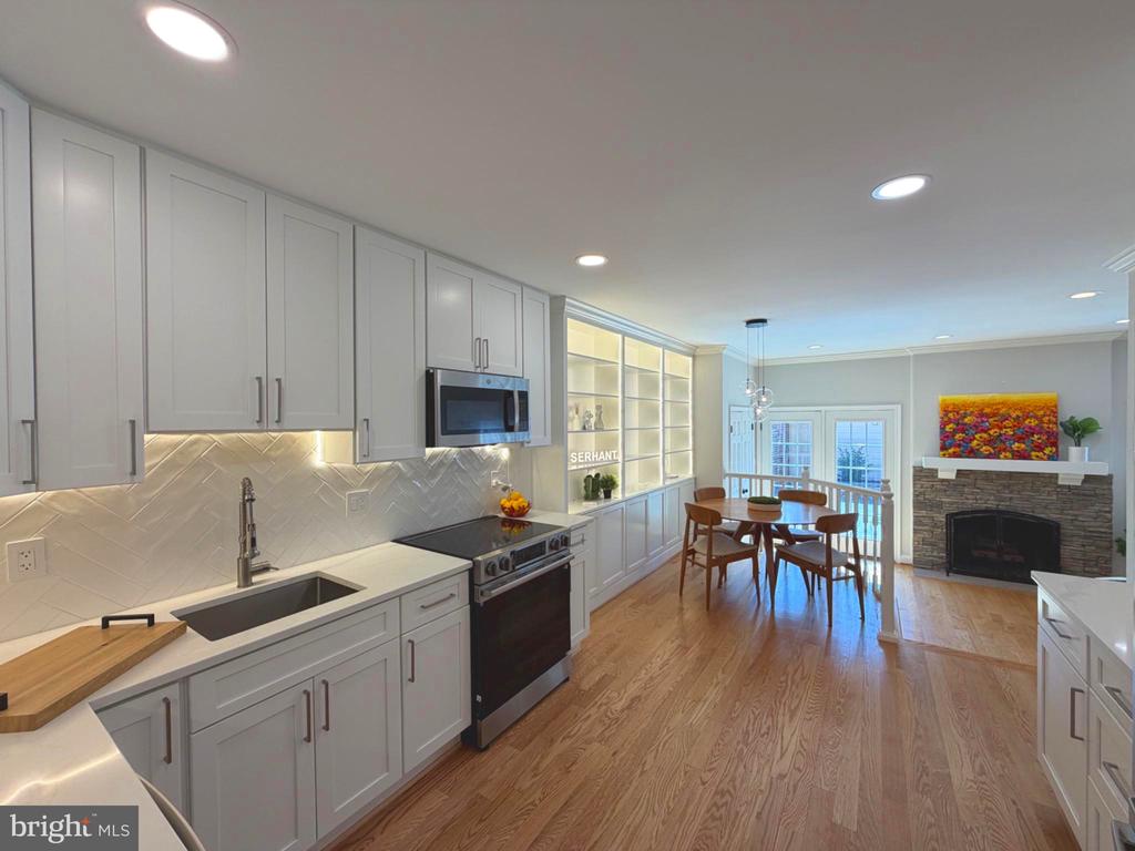 Kitchen with white shaker cabinets and herringbone backsplash opening into a dining area with a stone fireplace.