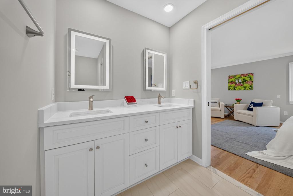 Bathroom with a white double-sink vanity and mirrors beside an open doorway to a sitting area.