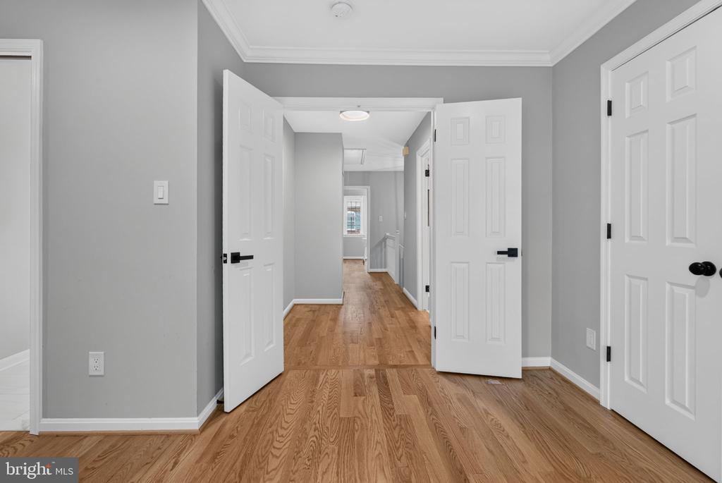 Unfurnished hallway with hardwood floors, gray walls, and several open white paneled doors.