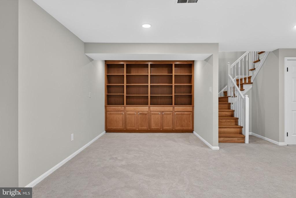 Carpeted room with a built-in wooden bookcase and staircase.