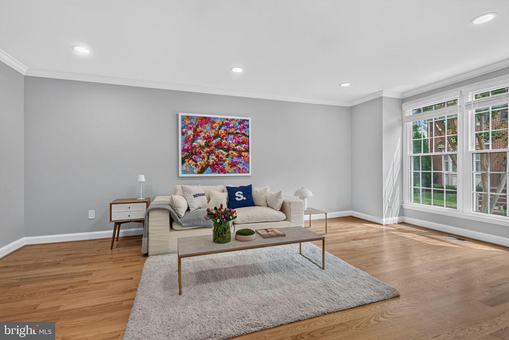 Living room with a cream sofa, colorful floral artwork, and large windows.