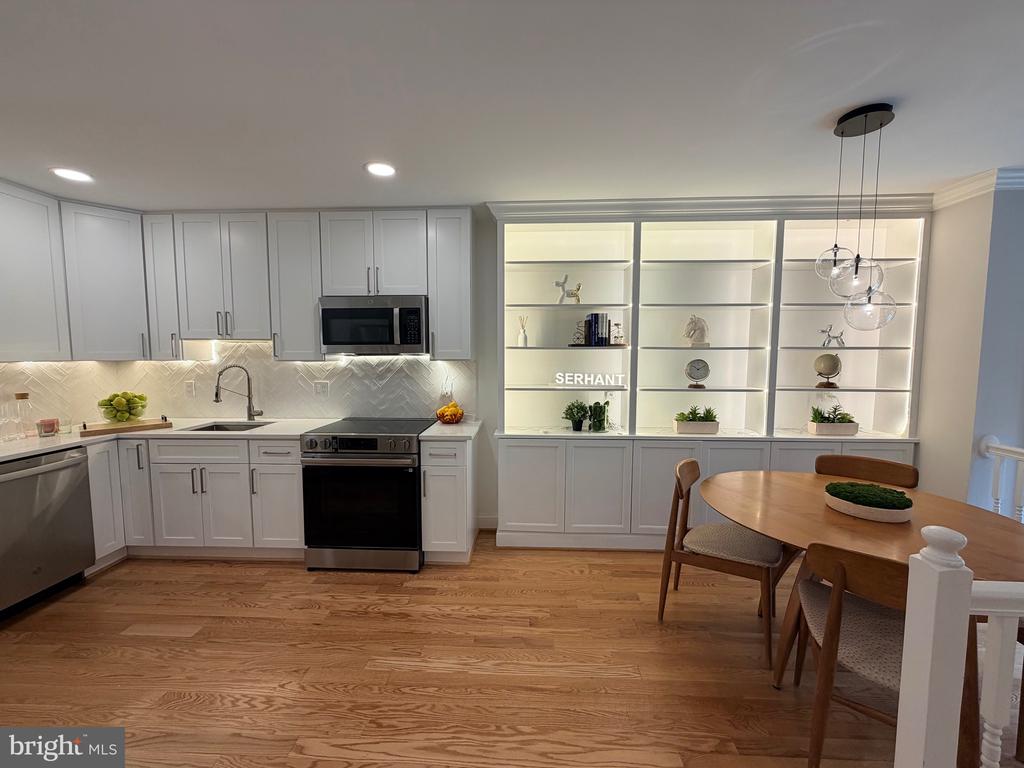 Kitchen with white cabinets, stainless steel appliances, illuminated display shelves, and a round wood dining table.