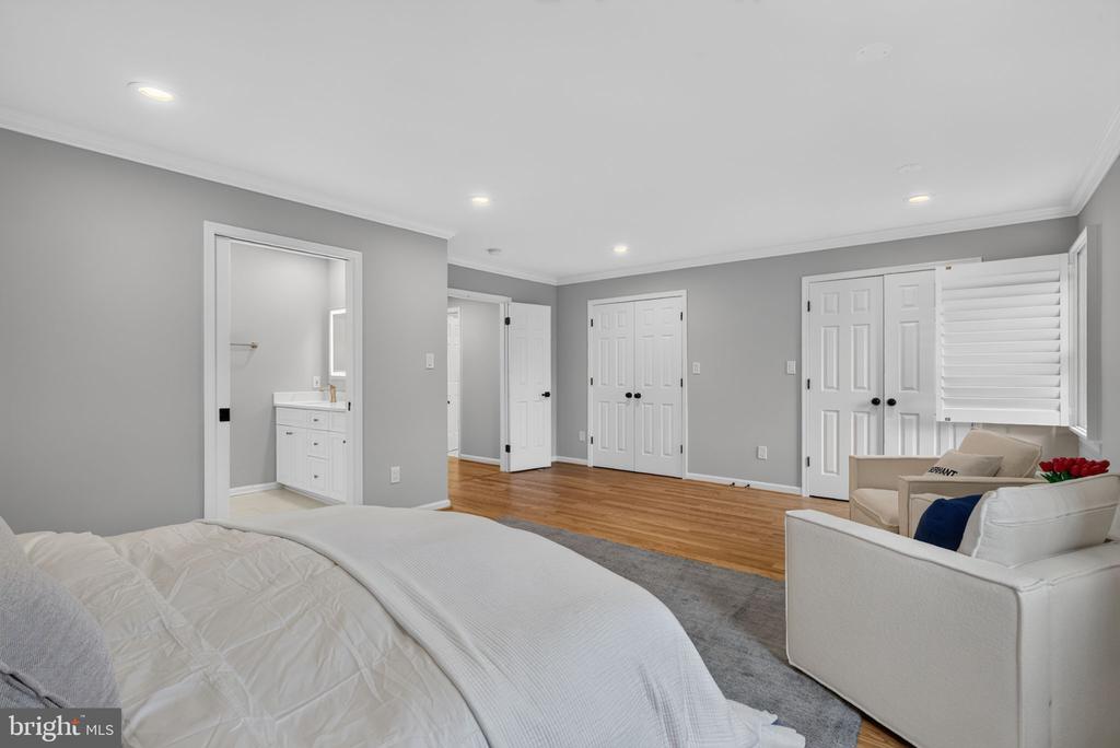 Staged bedroom with a white bed, hardwood floors, and an adjoining bathroom vanity.