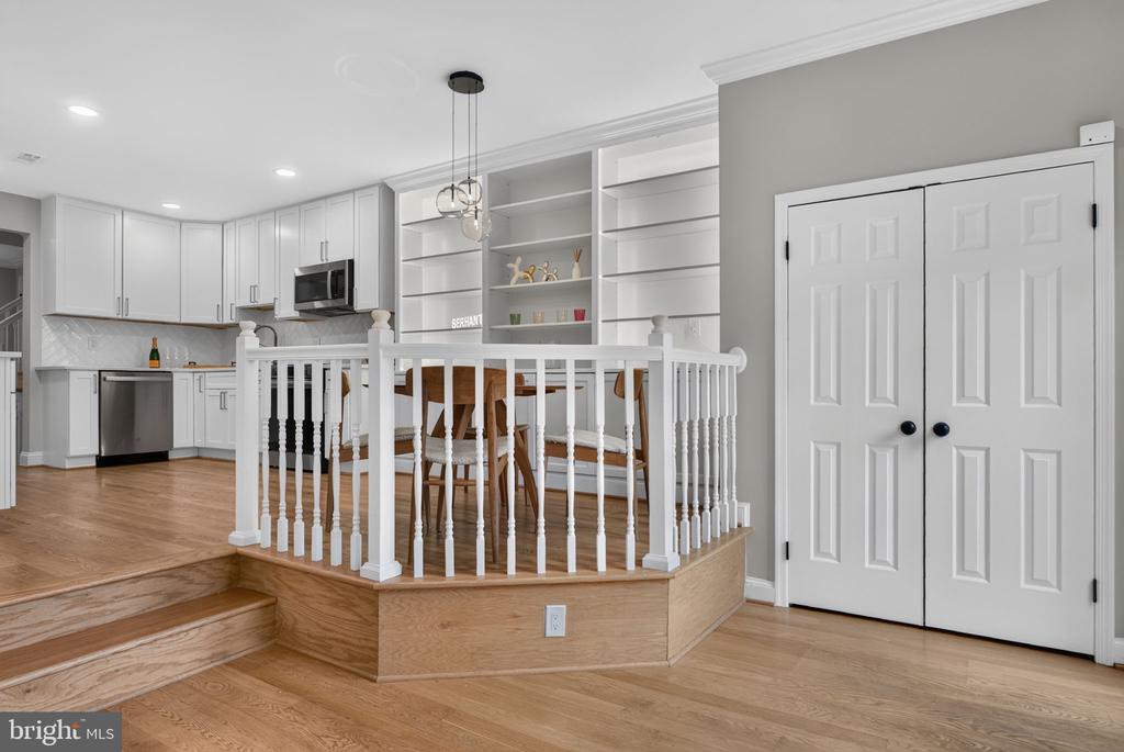 Kitchen and dining area with white cabinetry, built-in shelves, and a raised wood-floored platform.