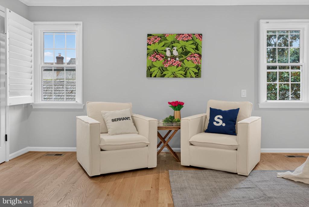 Staged living room with two cream armchairs, floral artwork, and bright windows.