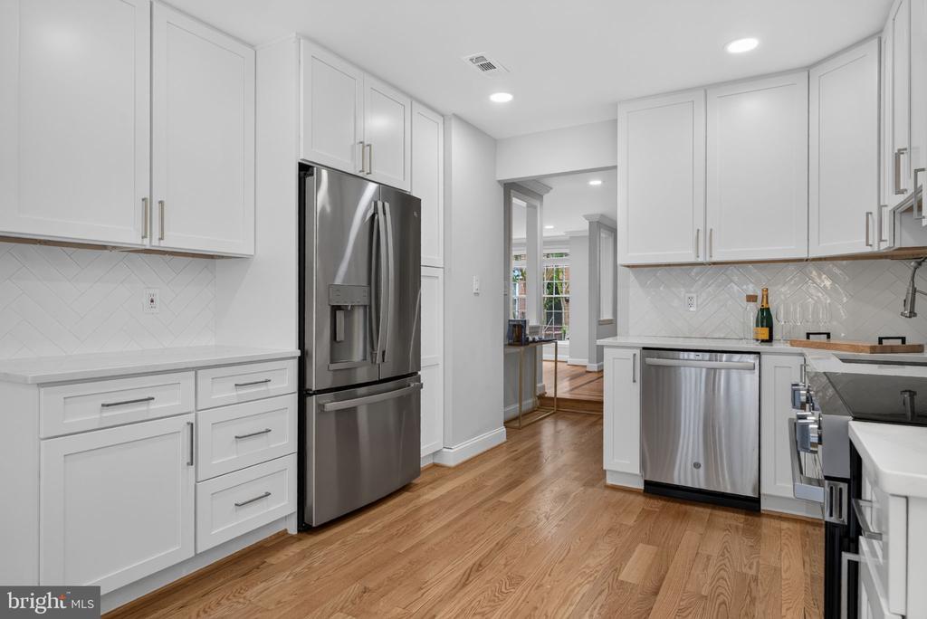Kitchen with white cabinets, stainless steel appliances, tile backsplash, and hardwood floors.