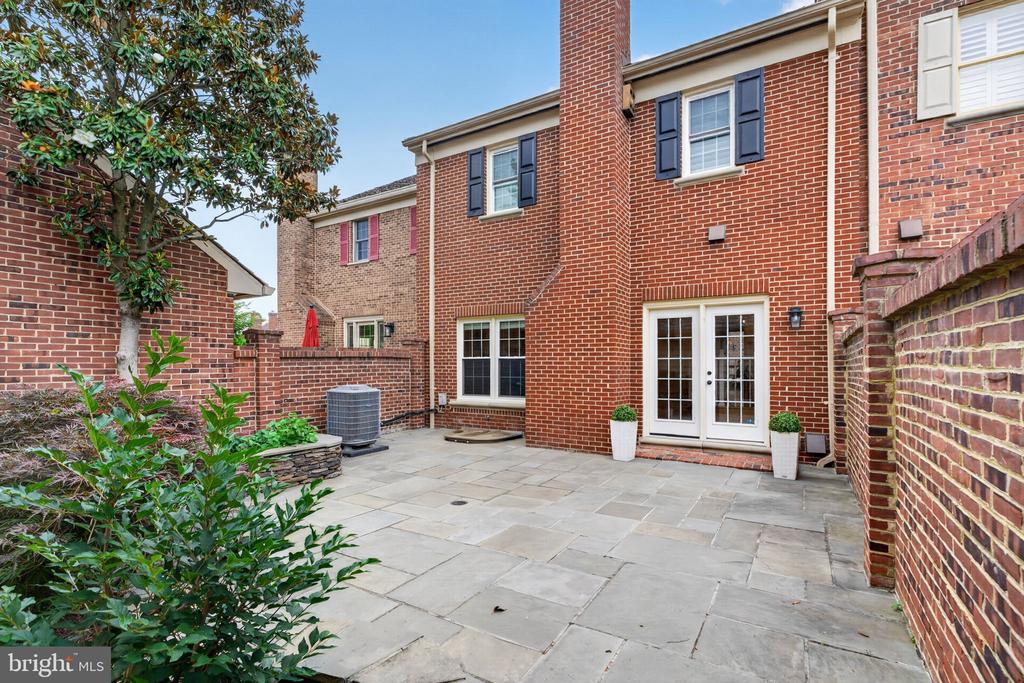 Stone-paved courtyard patio with brick walls, French doors, and leafy landscaping.