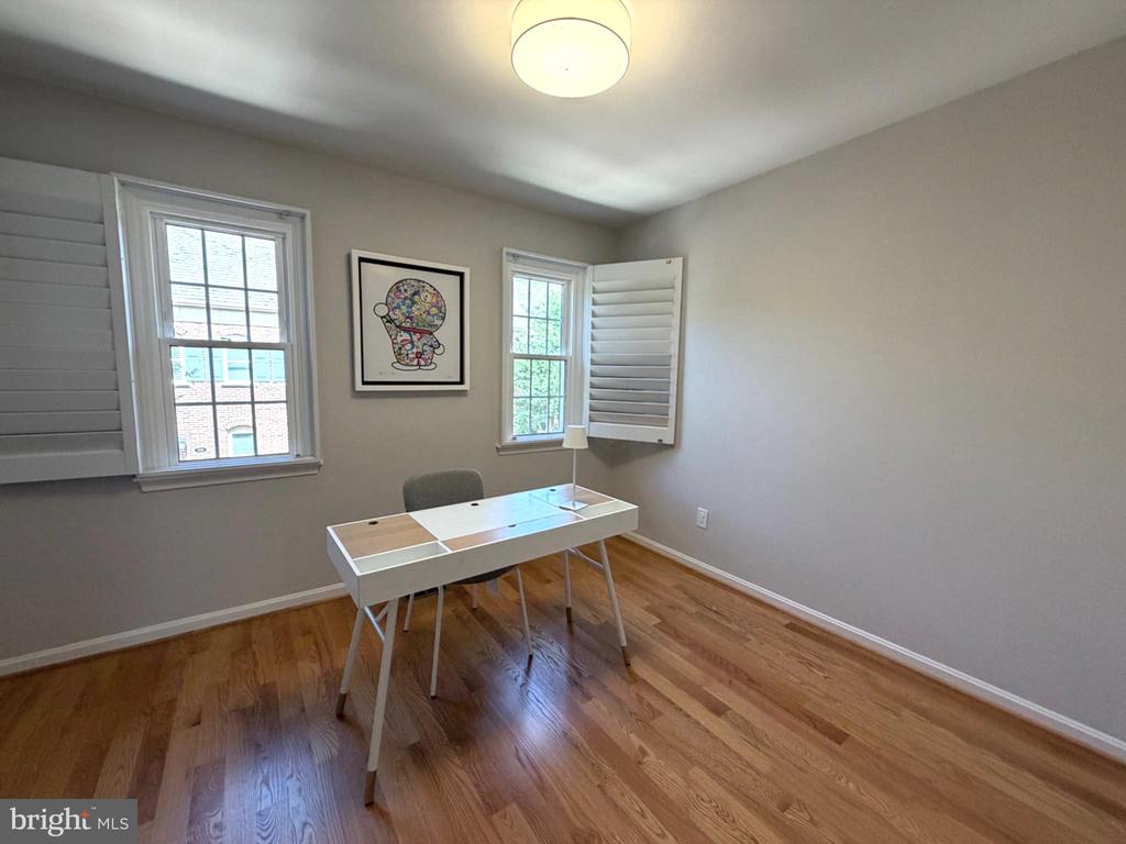 Home office with a white desk, hardwood floors, and two shuttered windows.