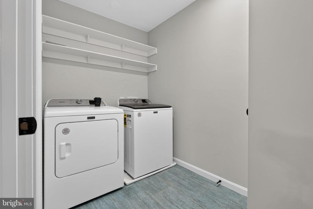 Laundry room with white washer and dryer beneath two wall shelves.