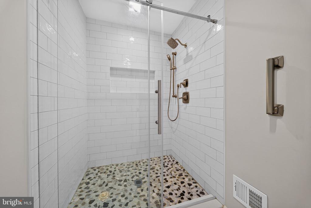 Walk-in shower with white subway tile, bronze fixtures, and a pebble mosaic floor.