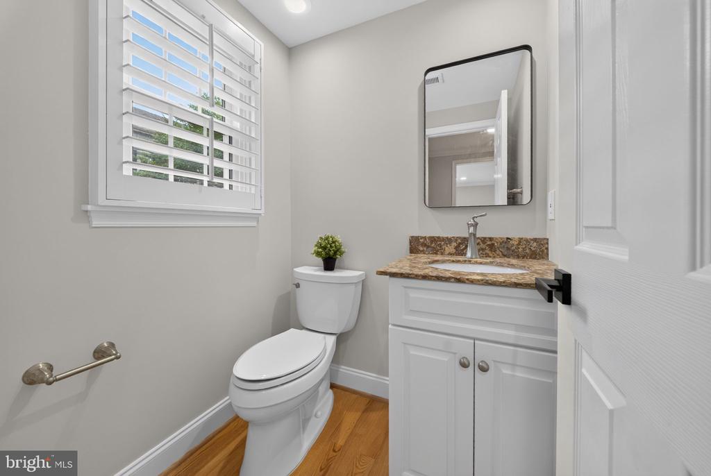 Bathroom with a white toilet, stone-counter vanity, rectangular mirror, and plantation shutters.