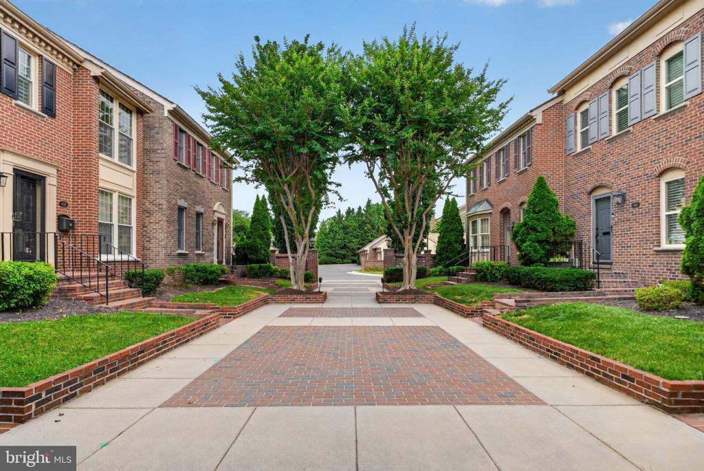 Brick townhomes frame a landscaped courtyard and brick walkway beneath mature trees.