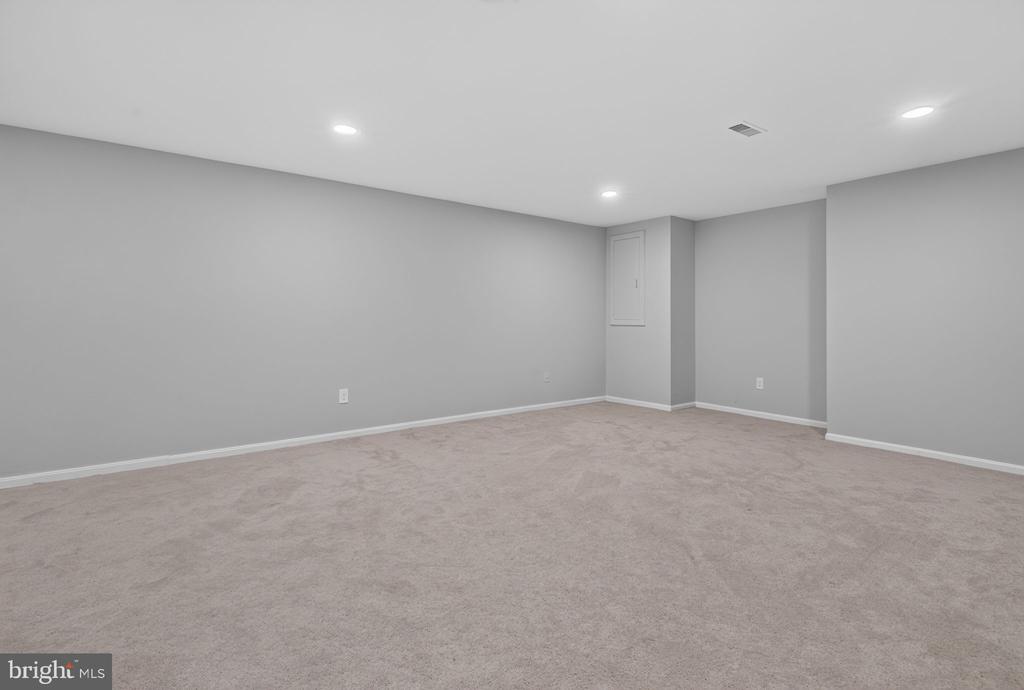 Empty carpeted basement room with gray walls and recessed ceiling lights.