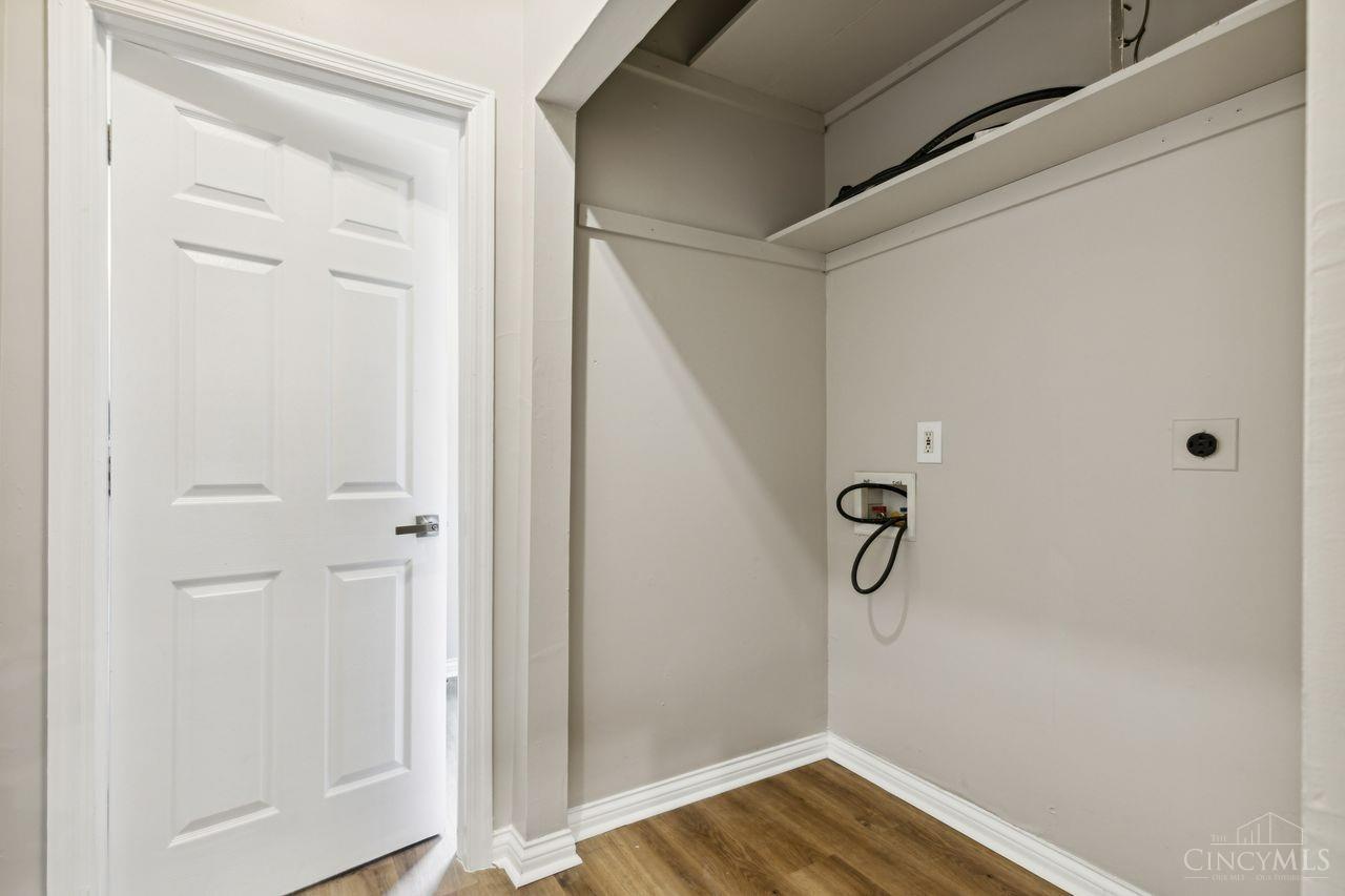 Empty laundry area with washer and dryer hookups, an overhead shelf, and a white paneled door.