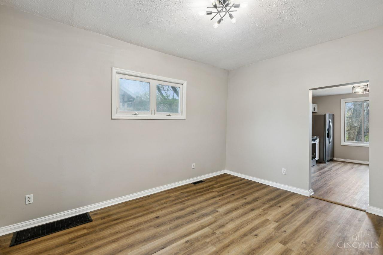 Vacant room with wood-look flooring, a small window, and an open doorway to the kitchen.