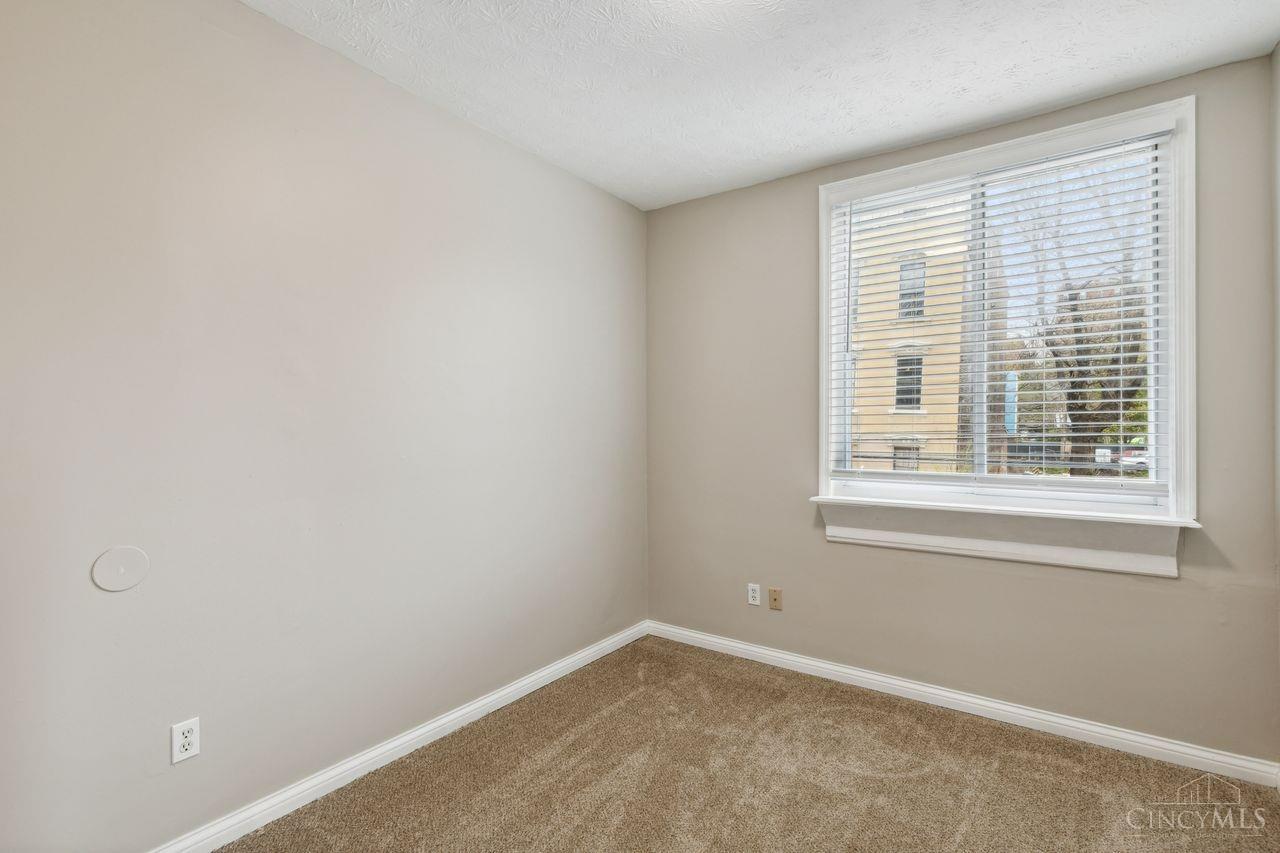 Vacant carpeted room with a large window and white blinds.