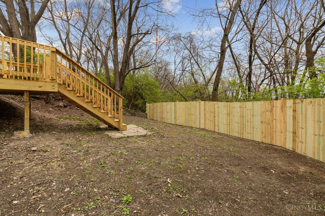 Backyard with raised wooden deck, stairs, and a new privacy fence beneath mature trees.