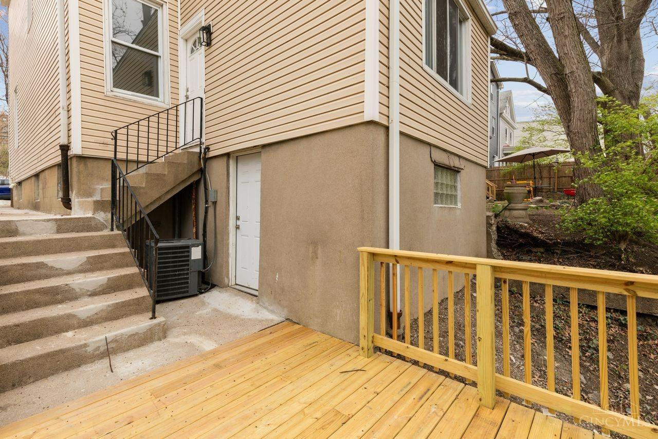 House exterior with concrete steps and a new wooden deck beside a fenced, tree-shaded yard.