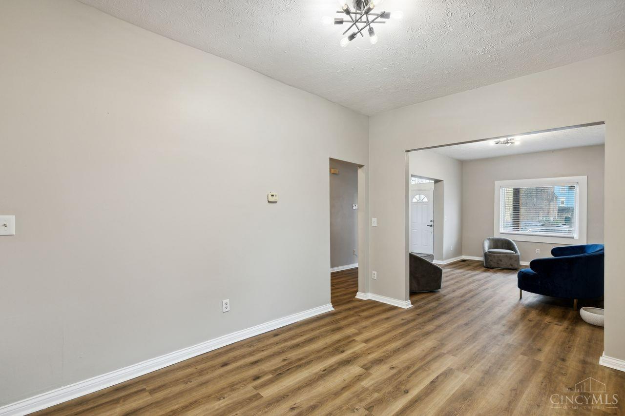 Open living area with wood-look floors, a high ceiling, and a furnished sitting area beyond.