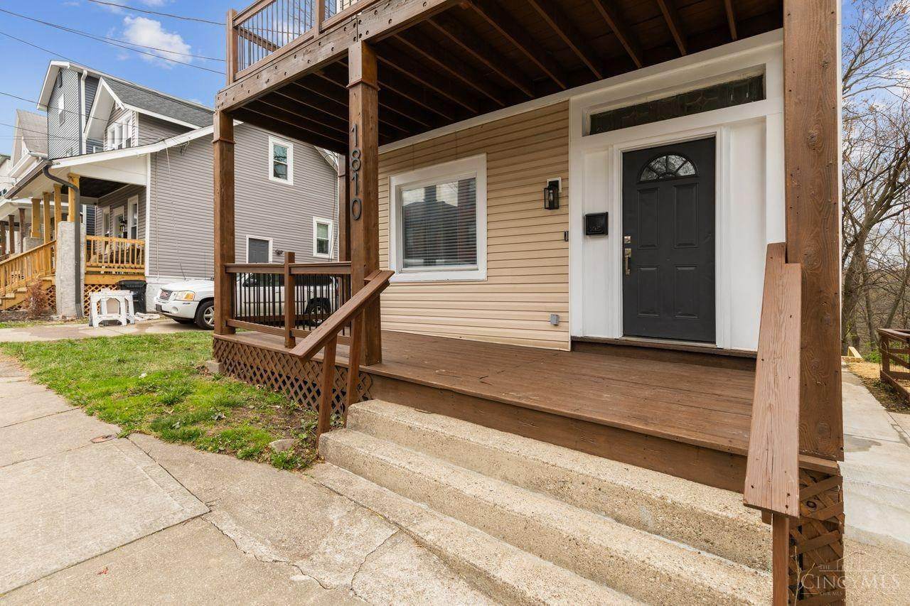 House exterior with a raised wooden porch, concrete steps, tan siding, and black front door.