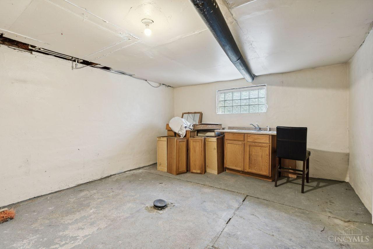 Unfinished basement with a concrete floor, exposed ductwork, and a sink with wooden cabinets.