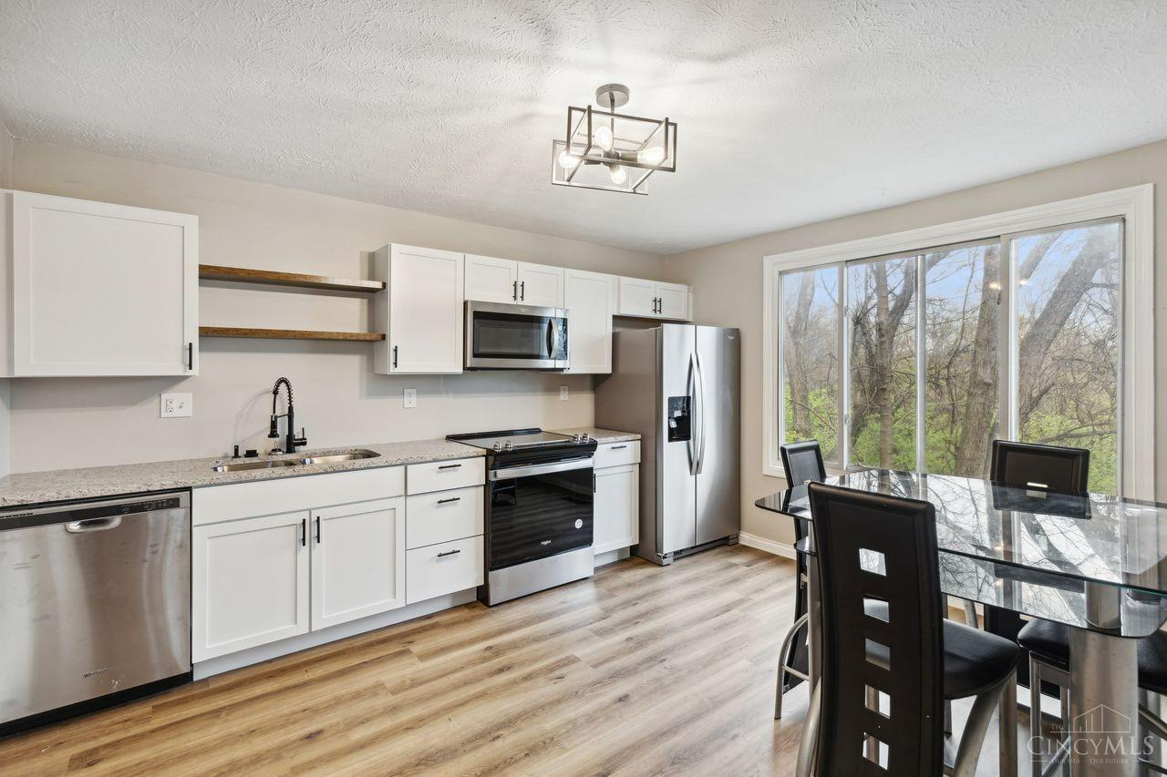 Kitchen with white cabinets and stainless appliances, opening to a glass dining table beside large windows.