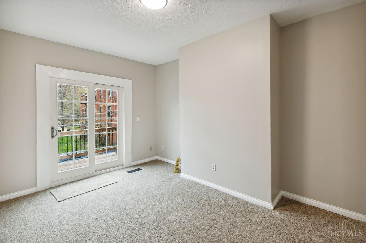 Empty carpeted room with white-trimmed glass doors opening to a small deck.