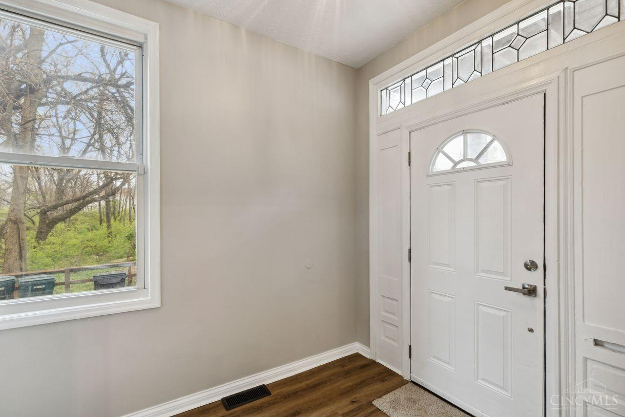 Entryway with a white front door, decorative glass transom, large window, and dark wood flooring.