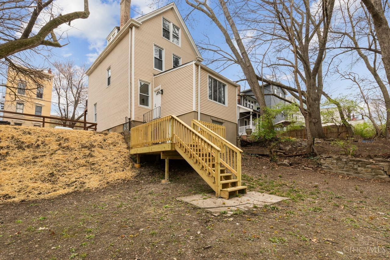 Rear exterior of a beige multi-story house with a raised wooden deck and stairs.