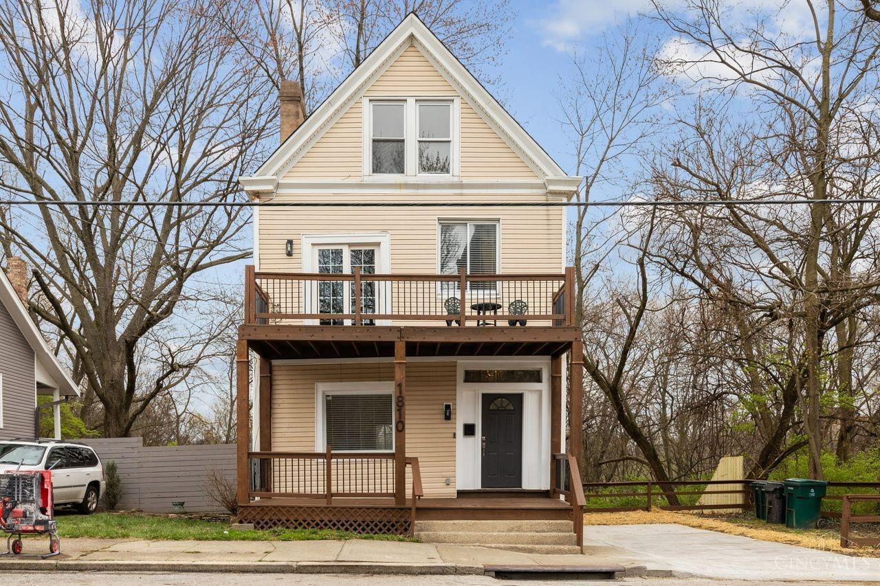 Tan gabled house with two levels of porches and a concrete driveway.