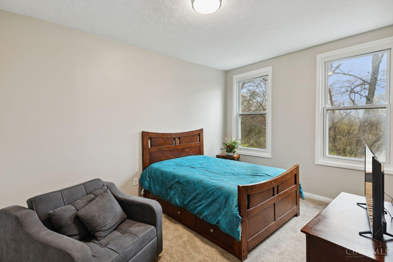 Bedroom with a wooden bed, turquoise bedding, gray loveseat, and two bright windows.