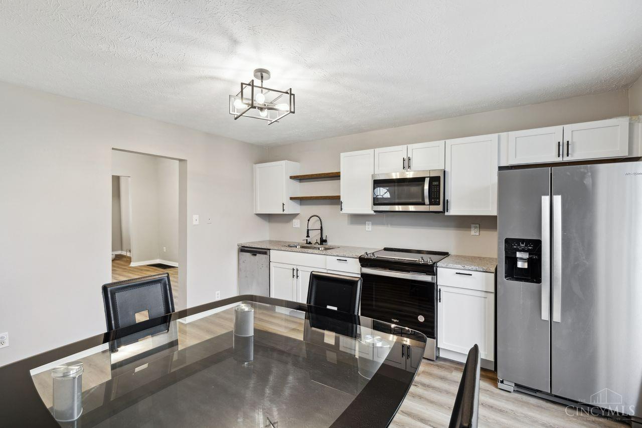 Kitchen and dining area with white cabinets, stainless steel appliances, and a dark glass dining table.