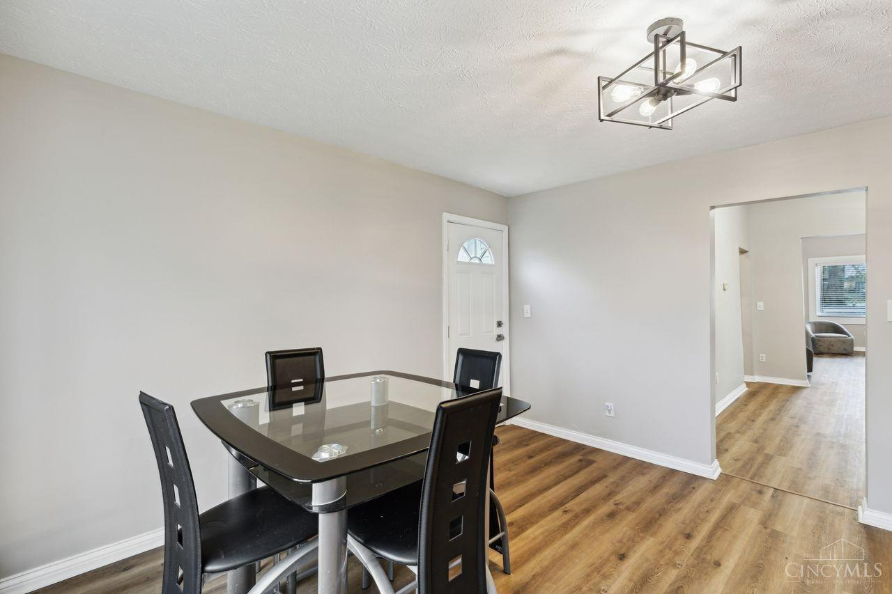 Dining room with a glass-top table, black chairs, wood-look flooring, and a geometric ceiling light.