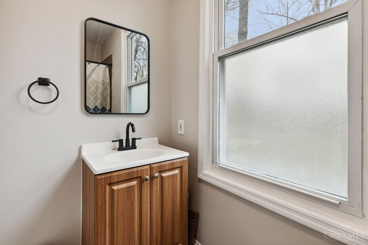 Bathroom vanity with a wood cabinet and black fixtures beside a large frosted window.