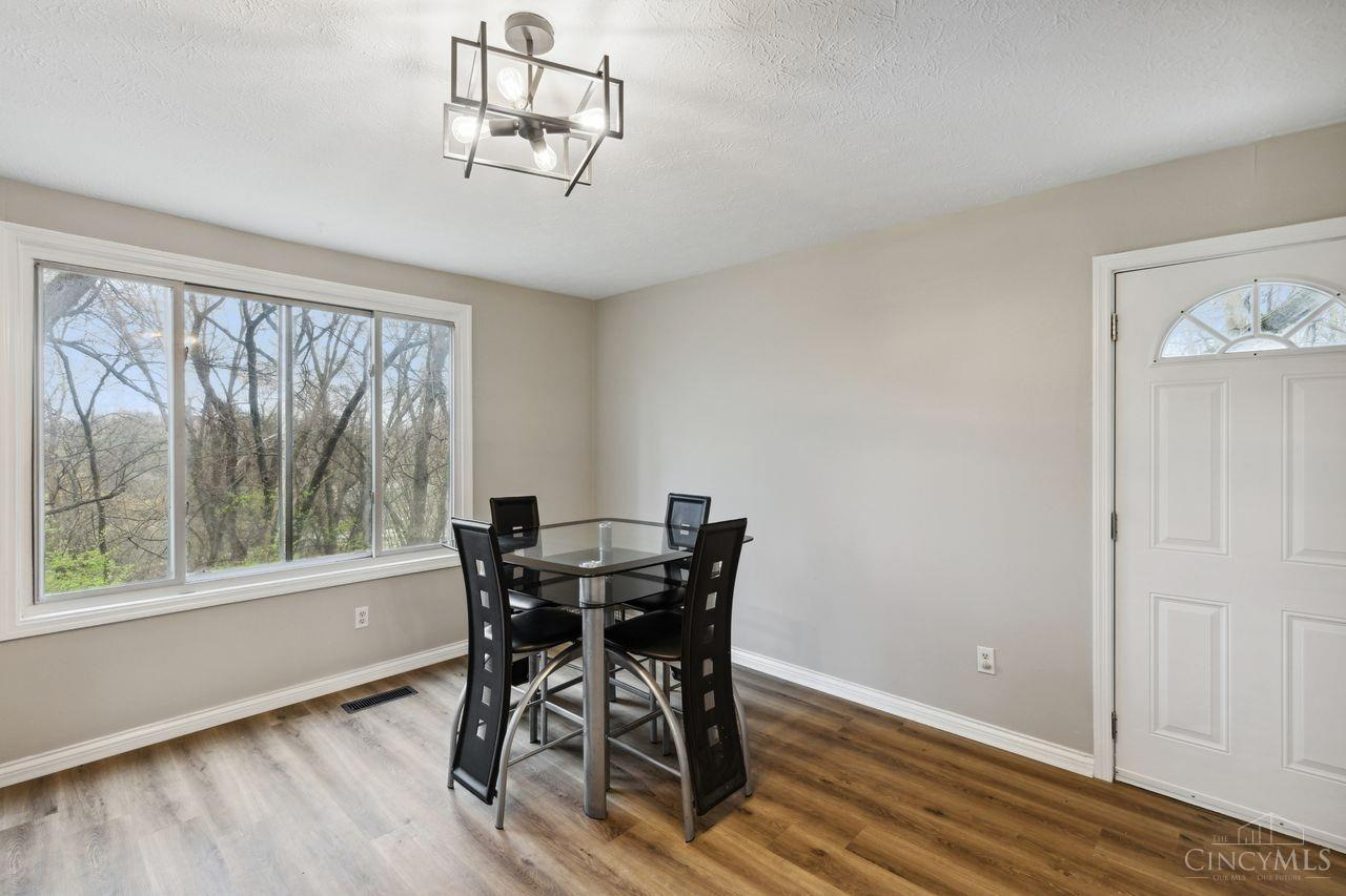 Dining room with a glass-top table, wide windows overlooking trees, and wood-look flooring.
