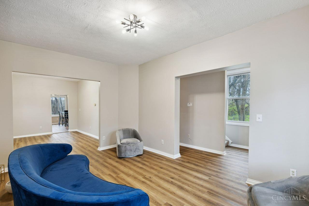 Living room with a curved blue sofa, gray chair, wood-look floors, and wide openings to adjoining rooms.