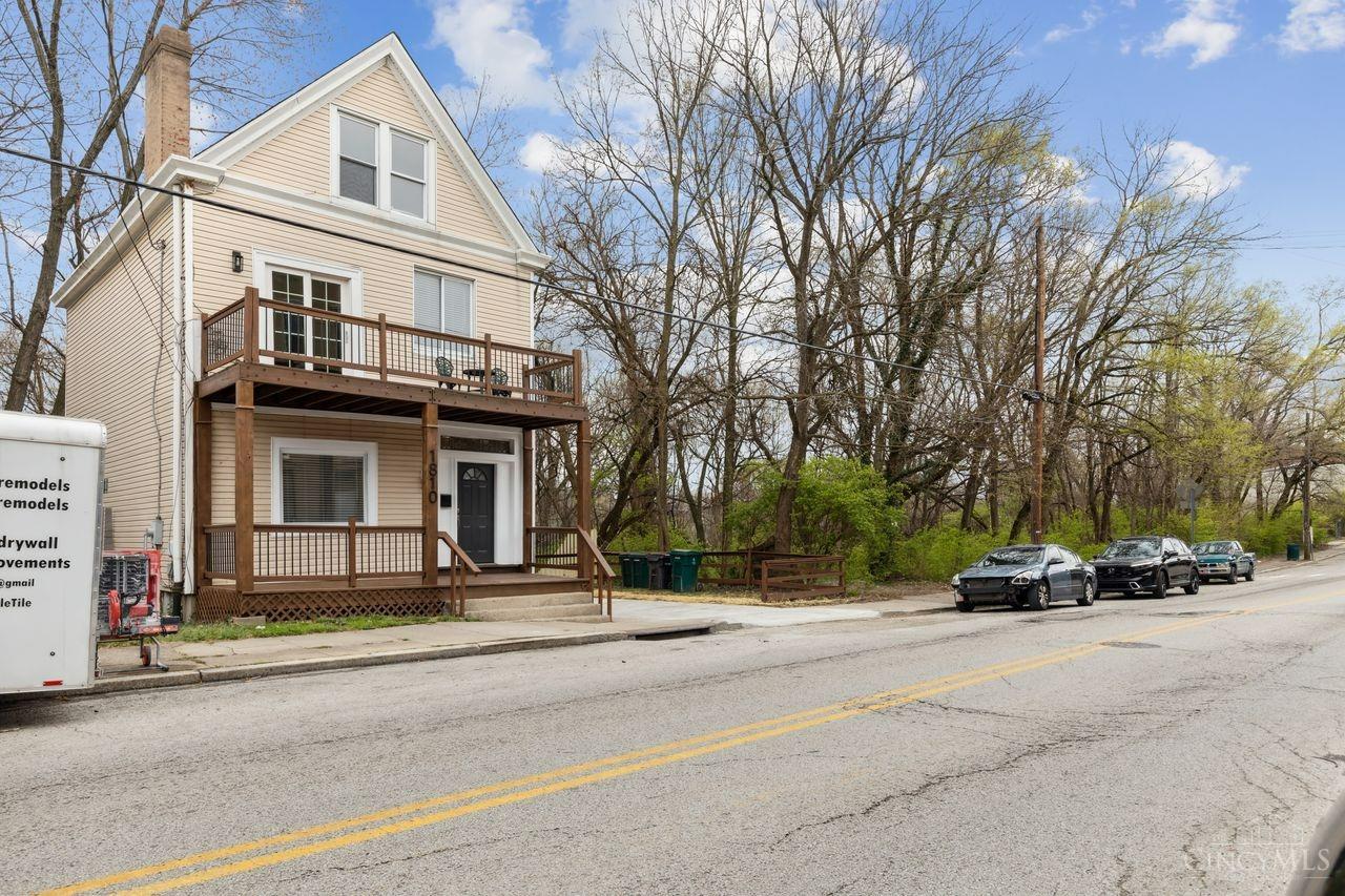Beige two-story house with a steep gable and wooden two-level porch facing the street.