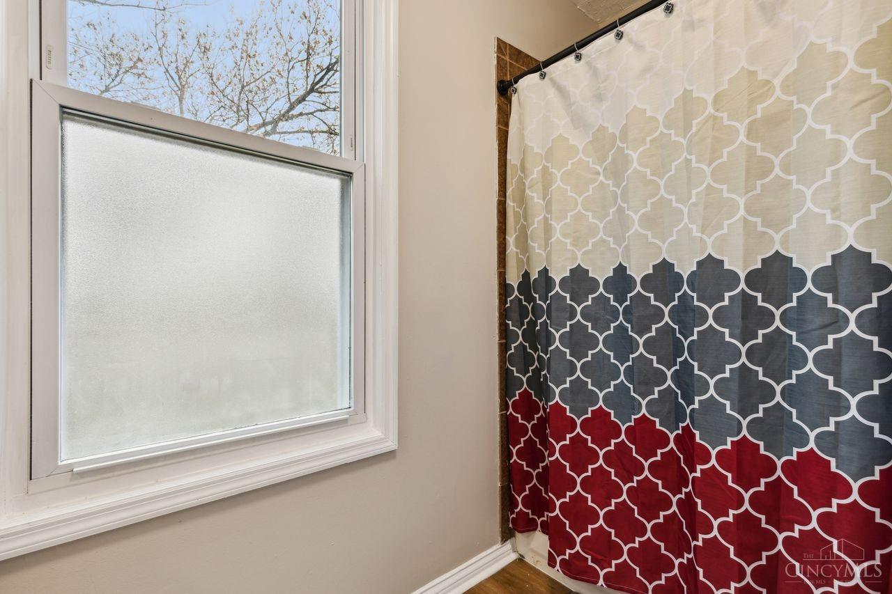 Bathroom window beside a cream, gray, and red patterned shower curtain.