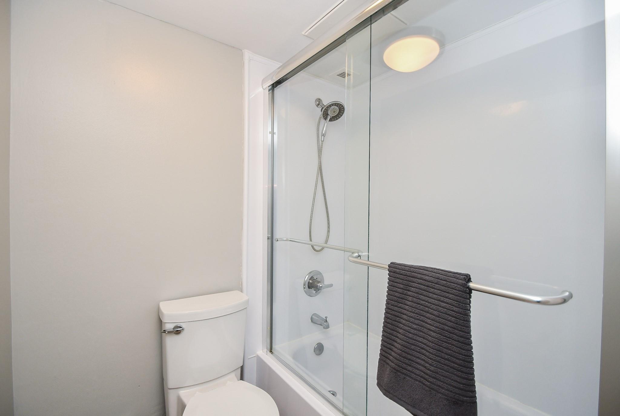 Bathroom with a glass-enclosed tub, handheld showerhead, and dark towel on the door handle.