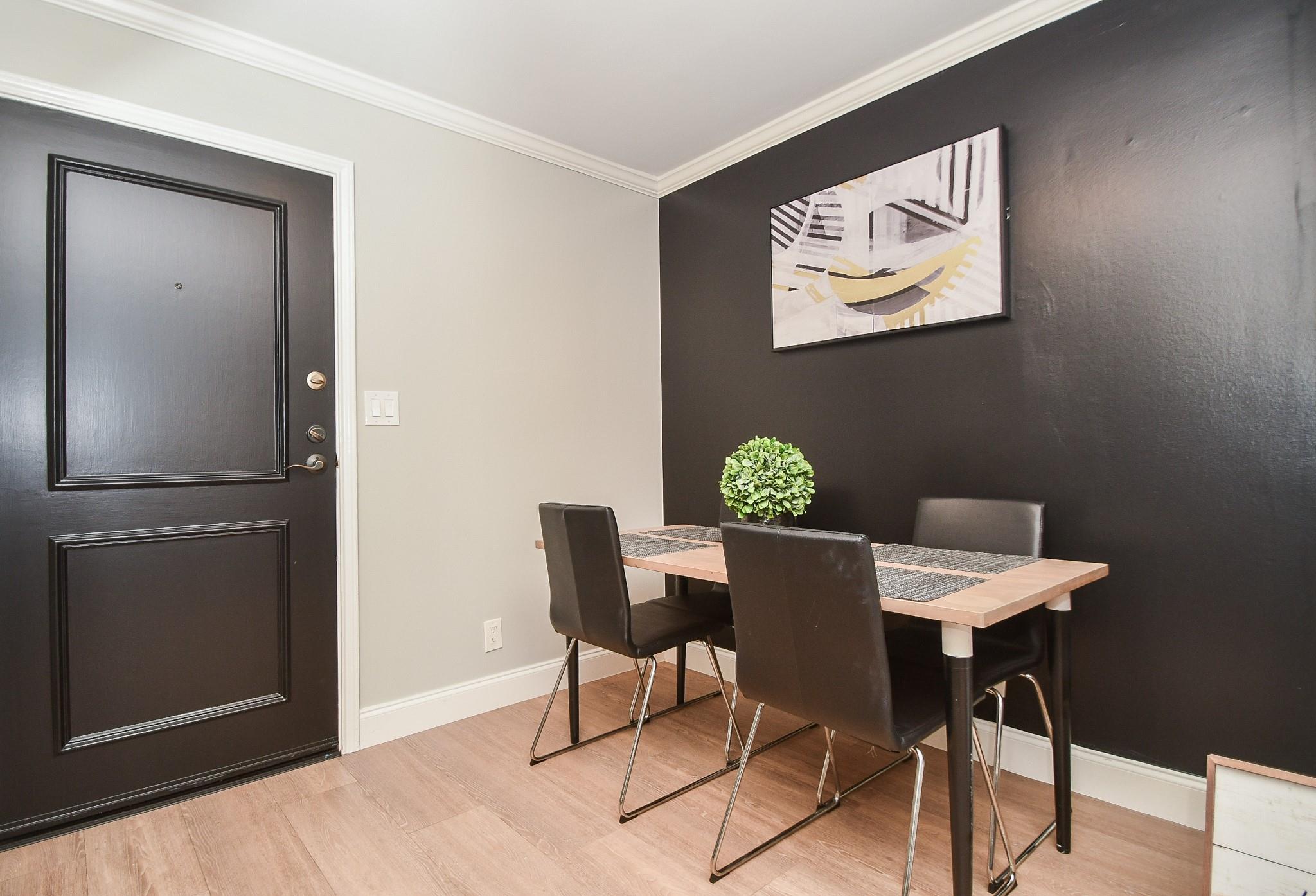 Dining area with a light wood table and black chairs beside a black paneled entry door.